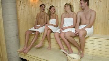 Un grupo de personas sentadas en bancos de madera en un sauna, con un balde y una cuchara de madera en el suelo.