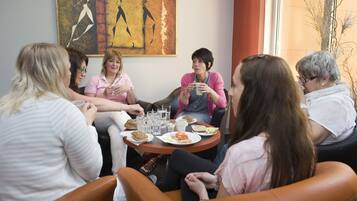 A group of people seated around a round table with food and drinks, in a room with a large abstract painting on the wall.