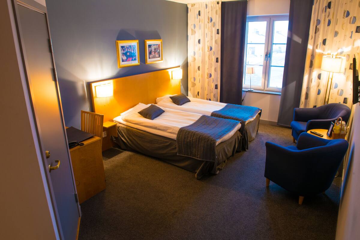 A hotel room with two beds, a desk, a chair, and a window with curtains.