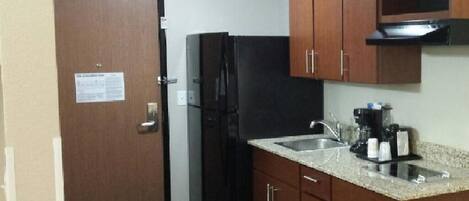 A compact kitchen with wooden cabinets, a black refrigerator, a sink, and a coffee maker.