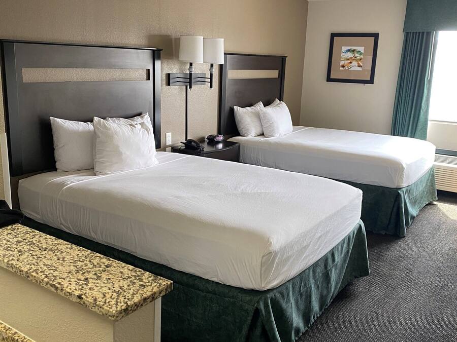 A hotel room with two beds, a desk, and a nightstand with lamps.