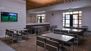A modern dining area with multiple tables and chairs, a large screen displaying a golf game, and large windows providing natural light. - Residence Inn Palo Alto Menlo Park (Menlo Park)