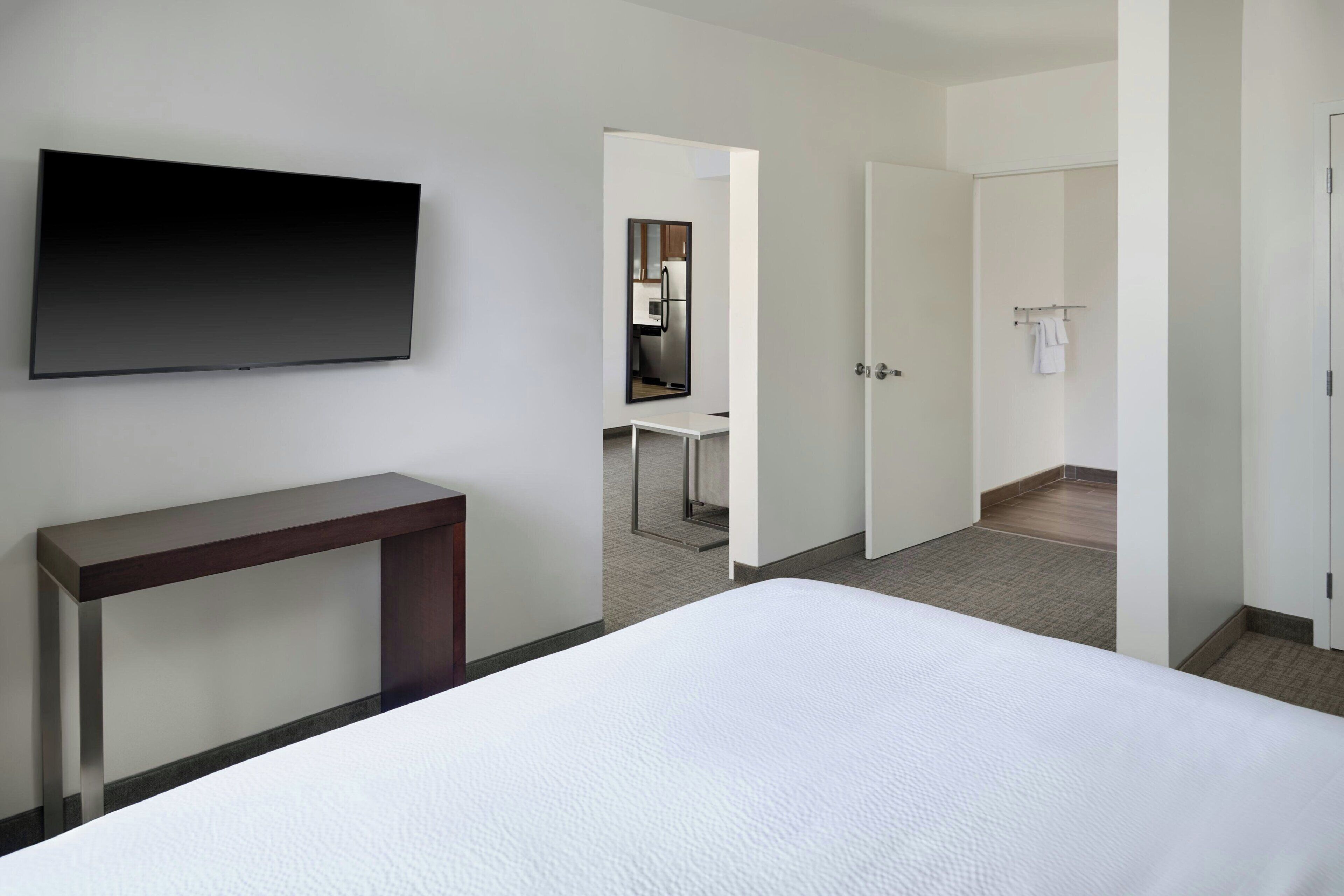 Habitación de hotel con una cama, televisión montada en la pared, un escritorio pequeño y una puerta que da al baño.