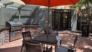 An outdoor patio with a grill, stone wall, and seating area under an umbrella. - Residence Inn Palo Alto Menlo Park (Menlo Park)