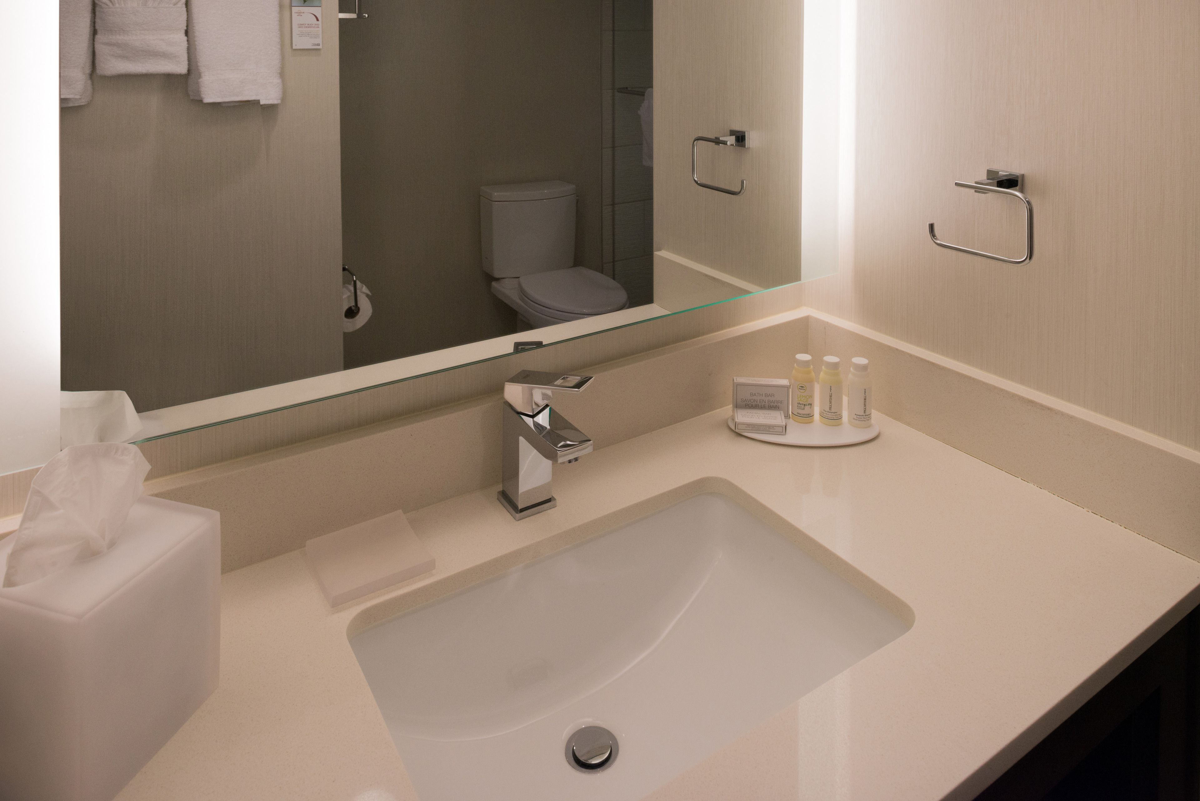 Un baño moderno con un espejo grande, un lavabo, un inodoro y un perchero para toallas.
