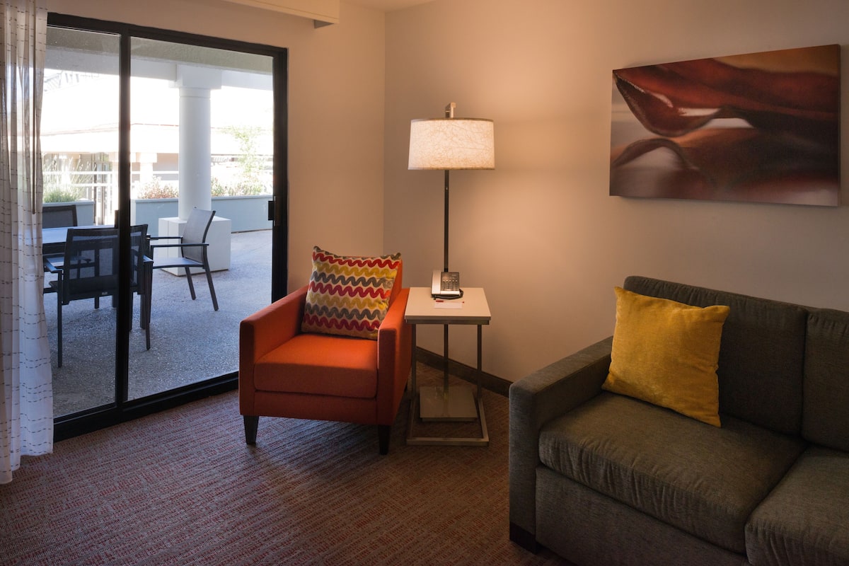 Ein Hotelzimmer mit Sofa, Sessel, Tisch, Lampe und einem Bild an der Wand.