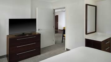 A hotel room with a bed, a dresser with drawers, a television, a mirror, and a door leading to another room.