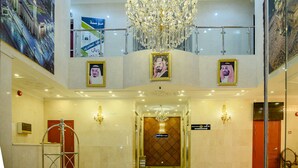 Um saguão de hotel com um lustre imponente, várias pinturas emolduradas e um balcão de recepção.