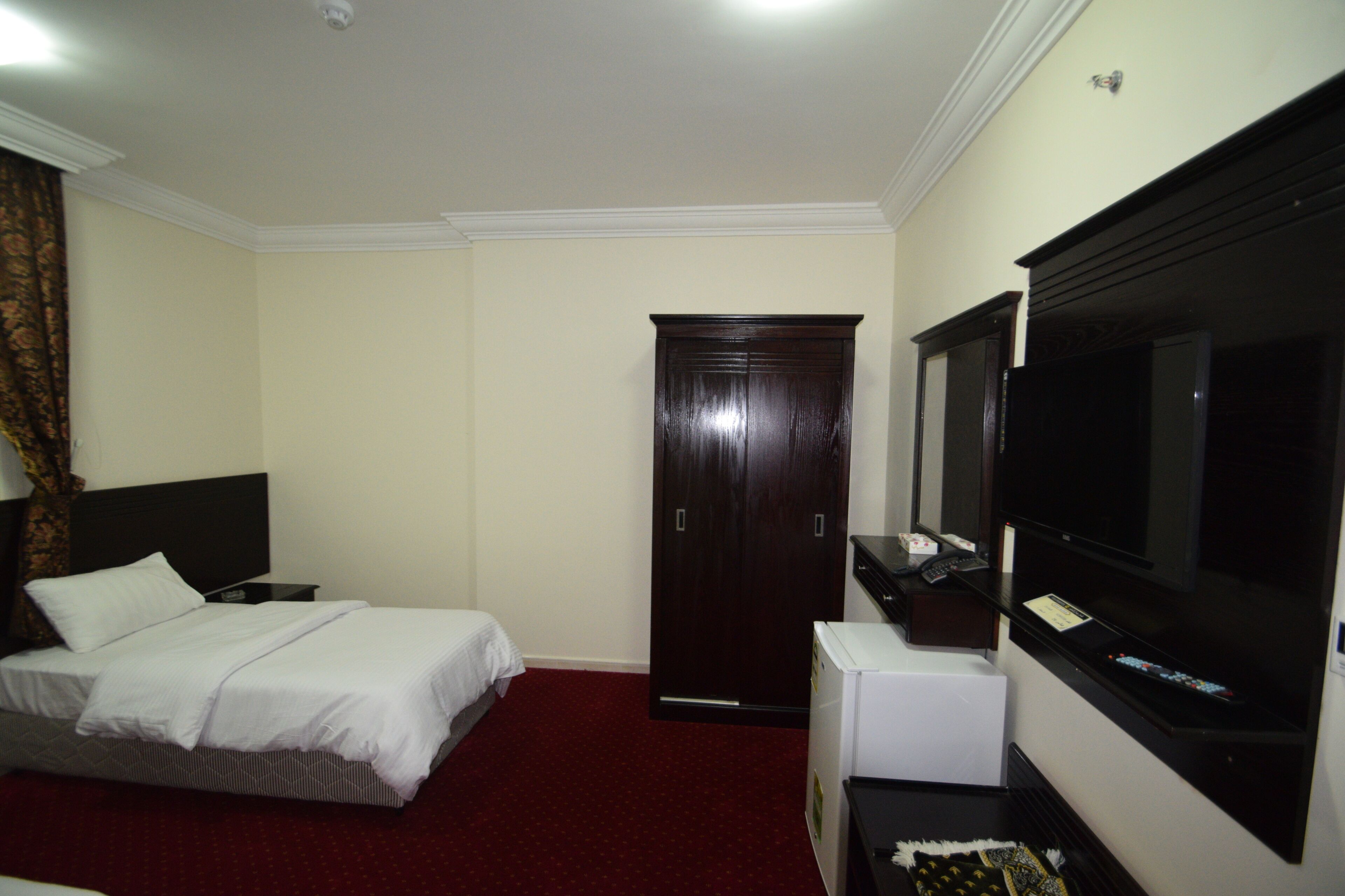 Una habitación de hotel con una cama, un armario, un televisor y un escritorio pequeño.