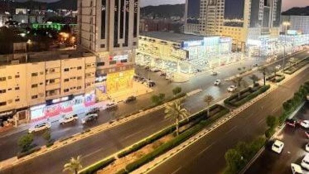 Um edifício alto com vários andares, rodeado por uma área urbana bem iluminada, com ruas e carros estacionados.