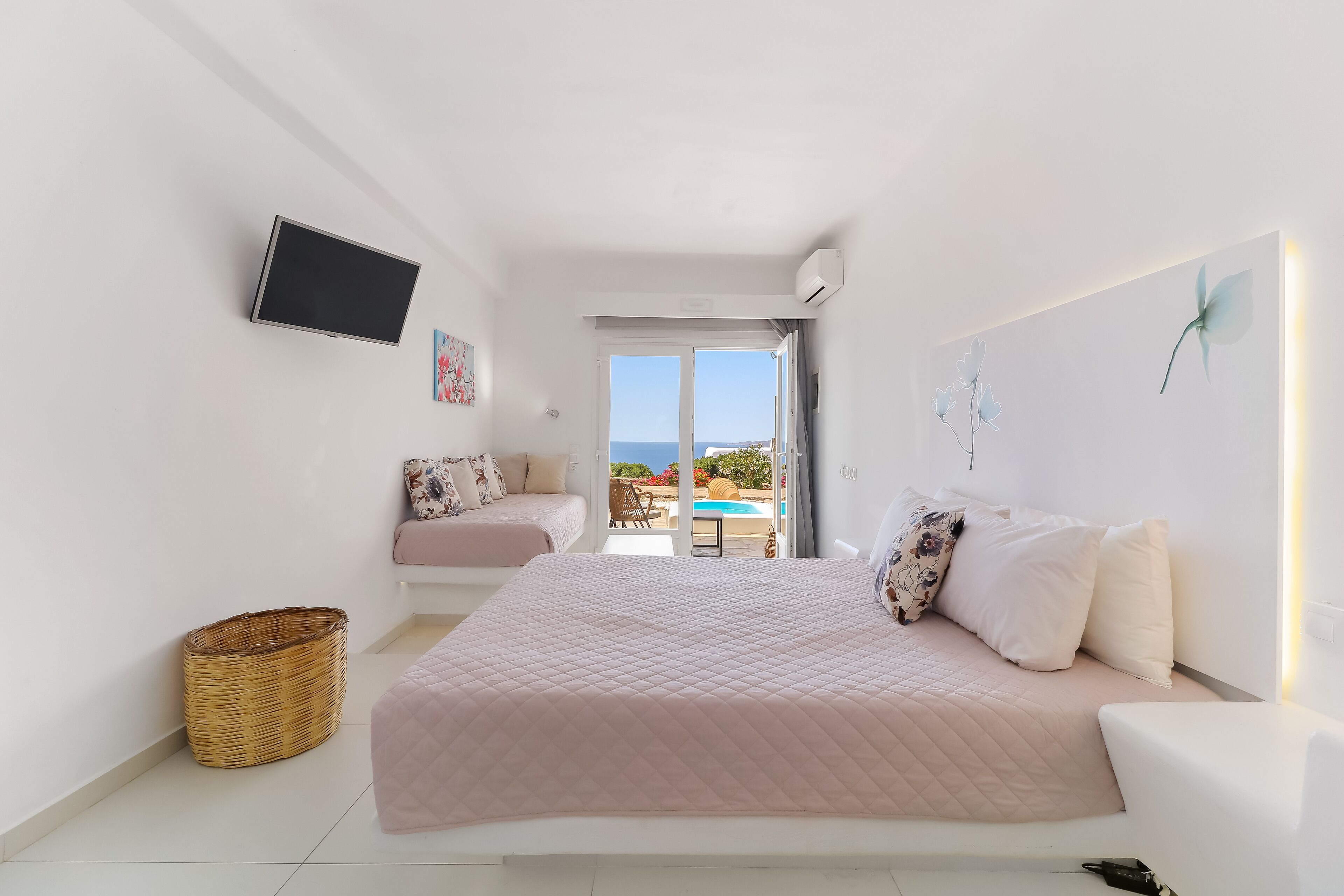 Ein Schlafzimmer mit einem großen Bett, einem an der Wand montierten Fernseher und Blick ins Freie.