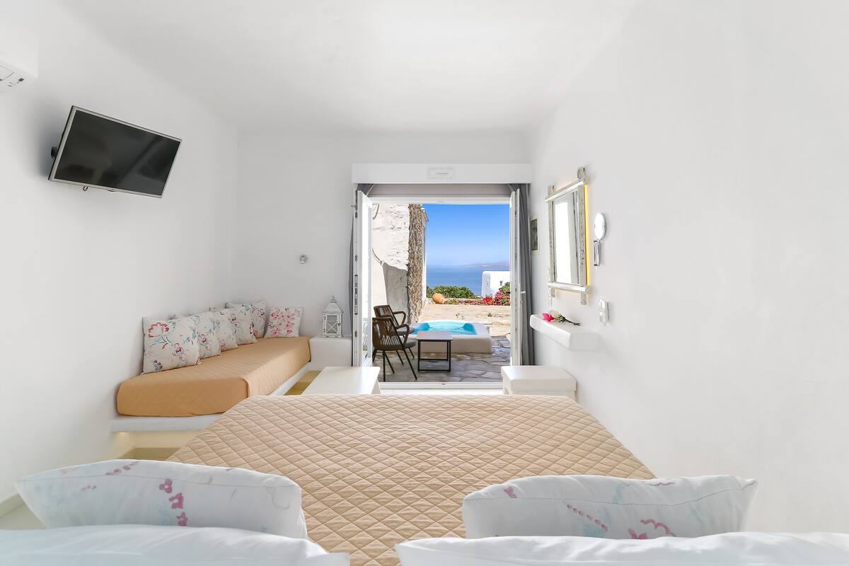 Un dormitorio con cama, televisión y vista al mar a través de una puerta abierta.