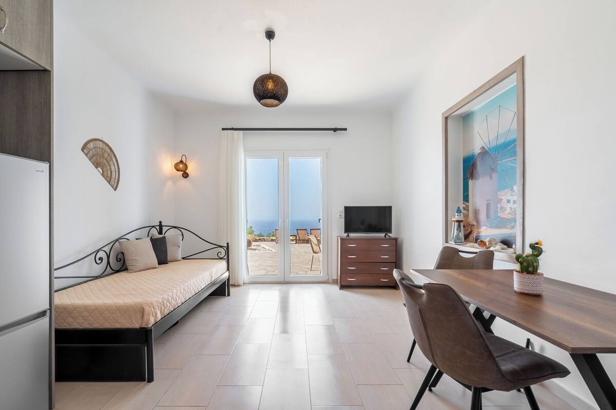 Un dormitorio moderno con cama, escritorio, silla, televisor y vista al mar.