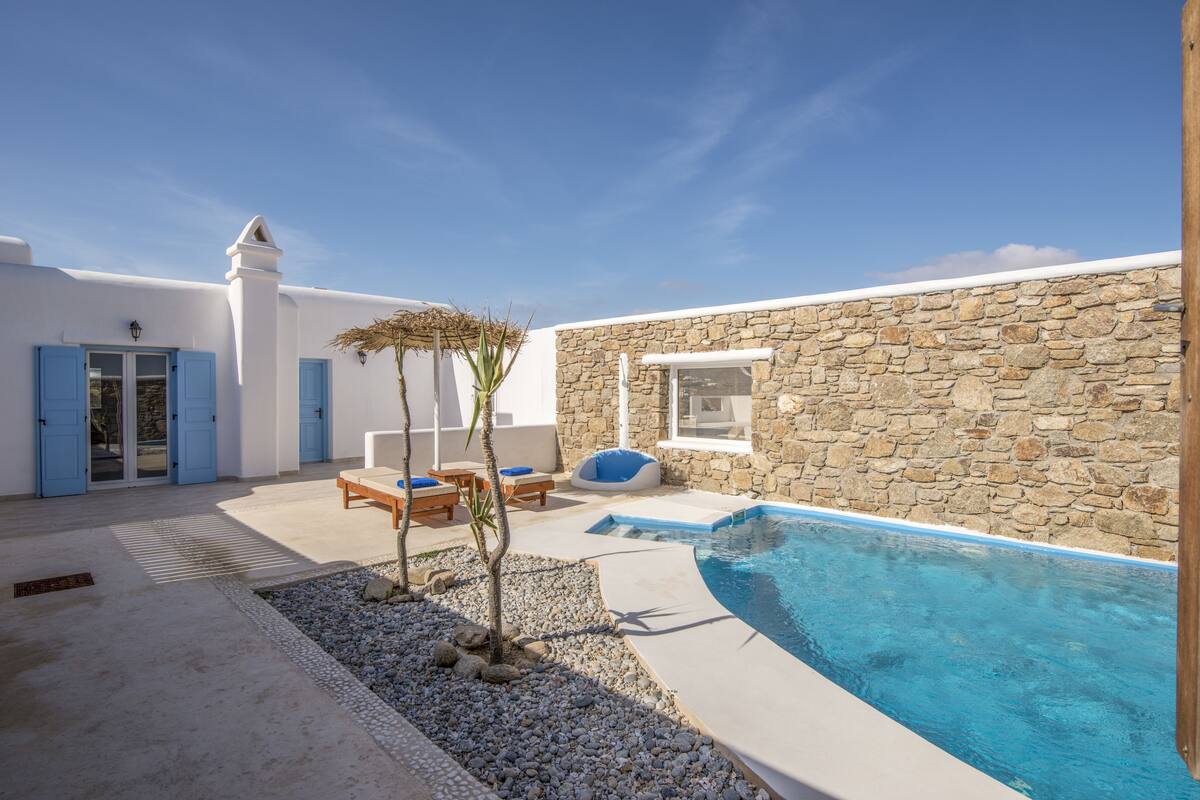 Zona junto a la piscina con pared de piedra, una pileta pequeña y mobiliario exterior.