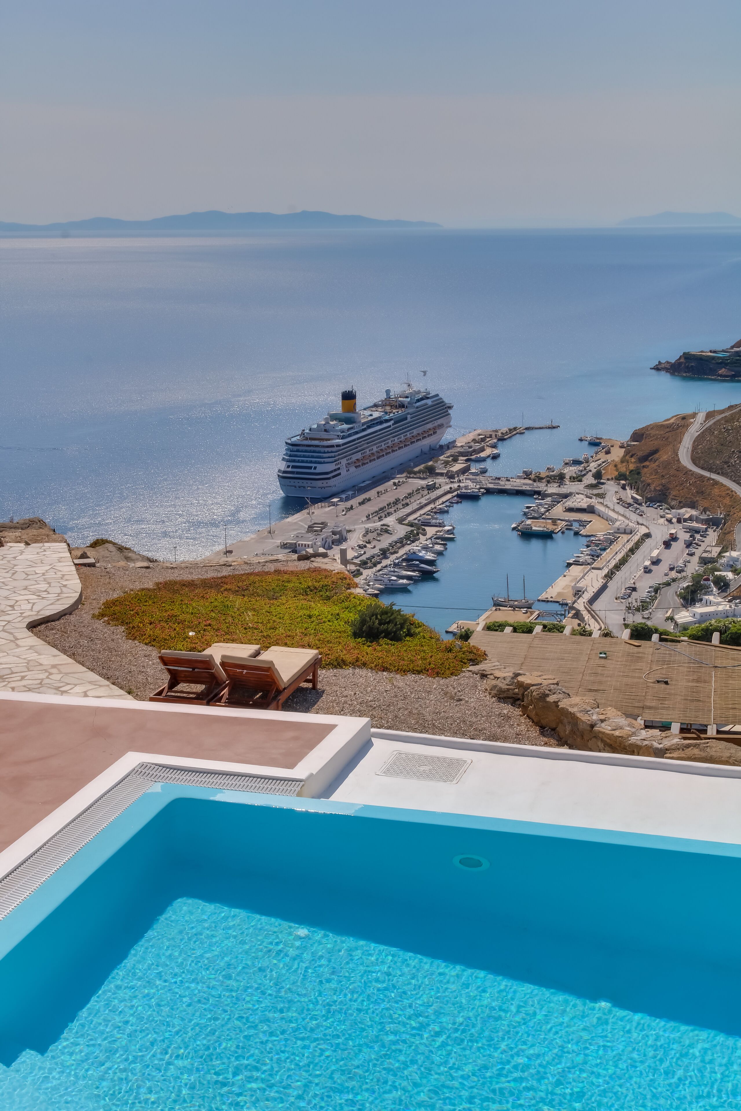 A pool area with a view of a cruise ship docked at a marina.