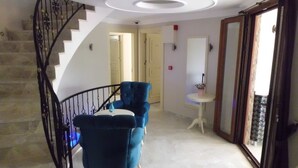 Una escalera con barandilla de metal negro, un sillón azul, una mesita redonda y una mesa blanca sobre pedestal.