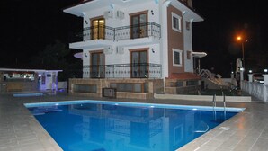 Un edificio de dos pisos con piscina, balcones y fachada iluminada.