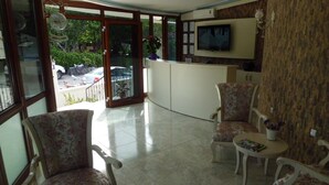 Un área de recepción con televisor, mostrador de recepción y zona de estar con sillones de estampado floral y una mesa pequeña.