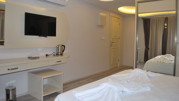 Habitación de hotel con cama, televisor montado en la pared, mesita de noche con hervidor, cubo de basura y espejo que refleja la habitación.