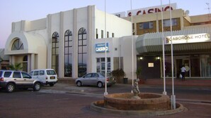 Un edificio de casino con un letrero llamativo, un estacionamiento con varios coches y una estatua al frente.