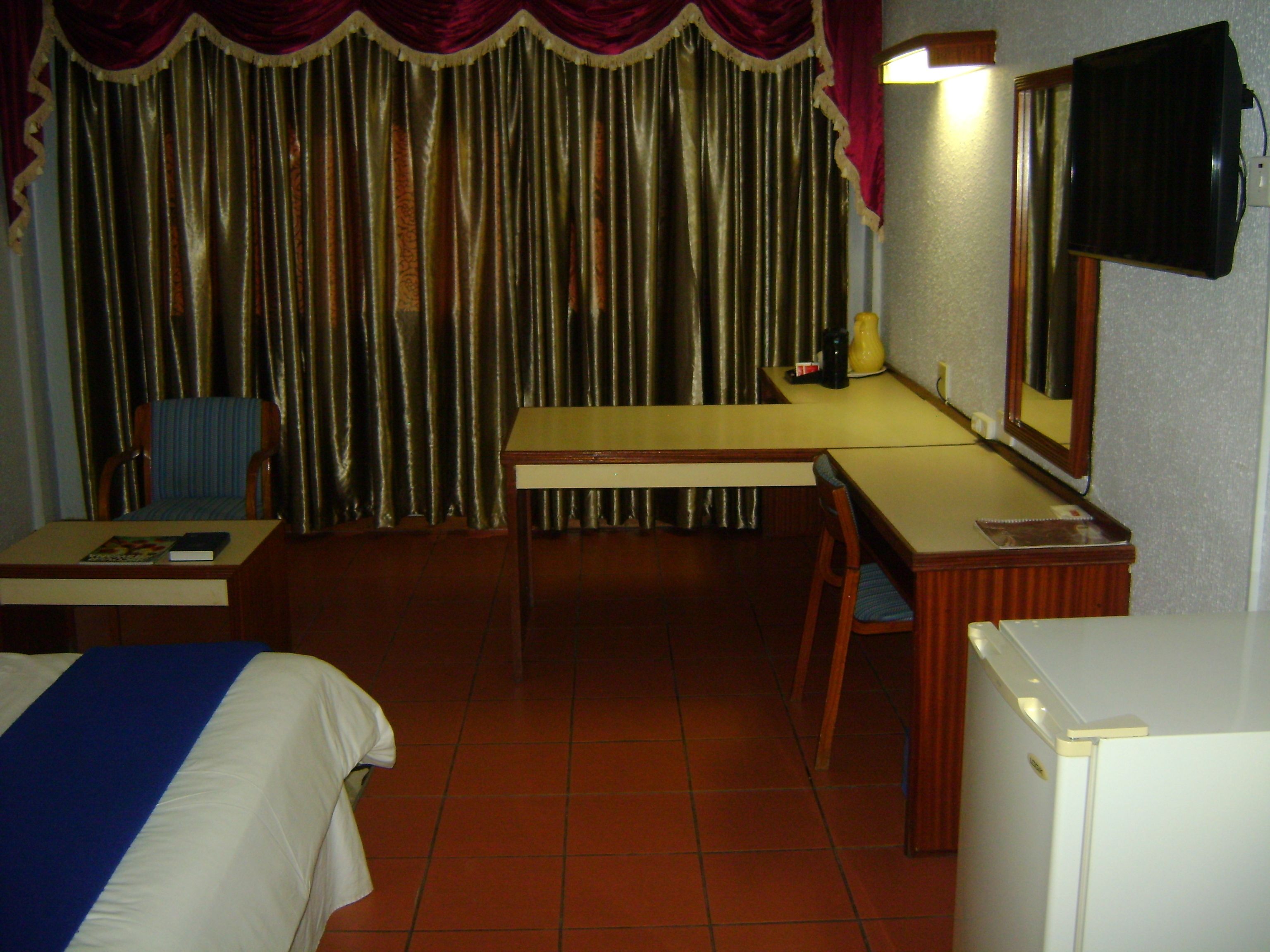 Habitación de hotel con cama, escritorio, silla, mesita, espejo y televisión.