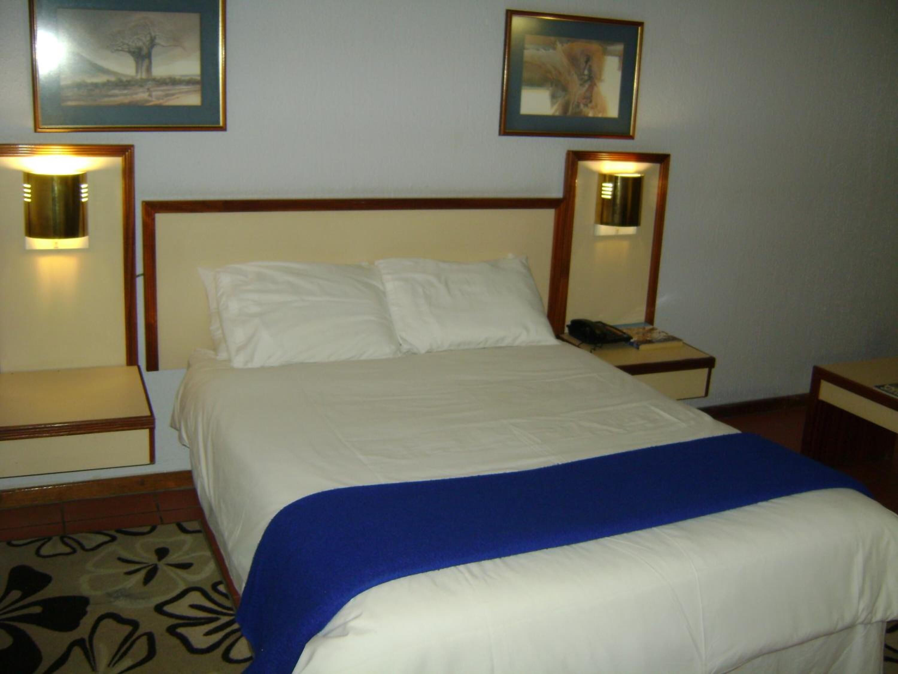 Habitación de hotel con cama, dos mesitas de noche, una mesita con teléfono y dos lámparas de pared.