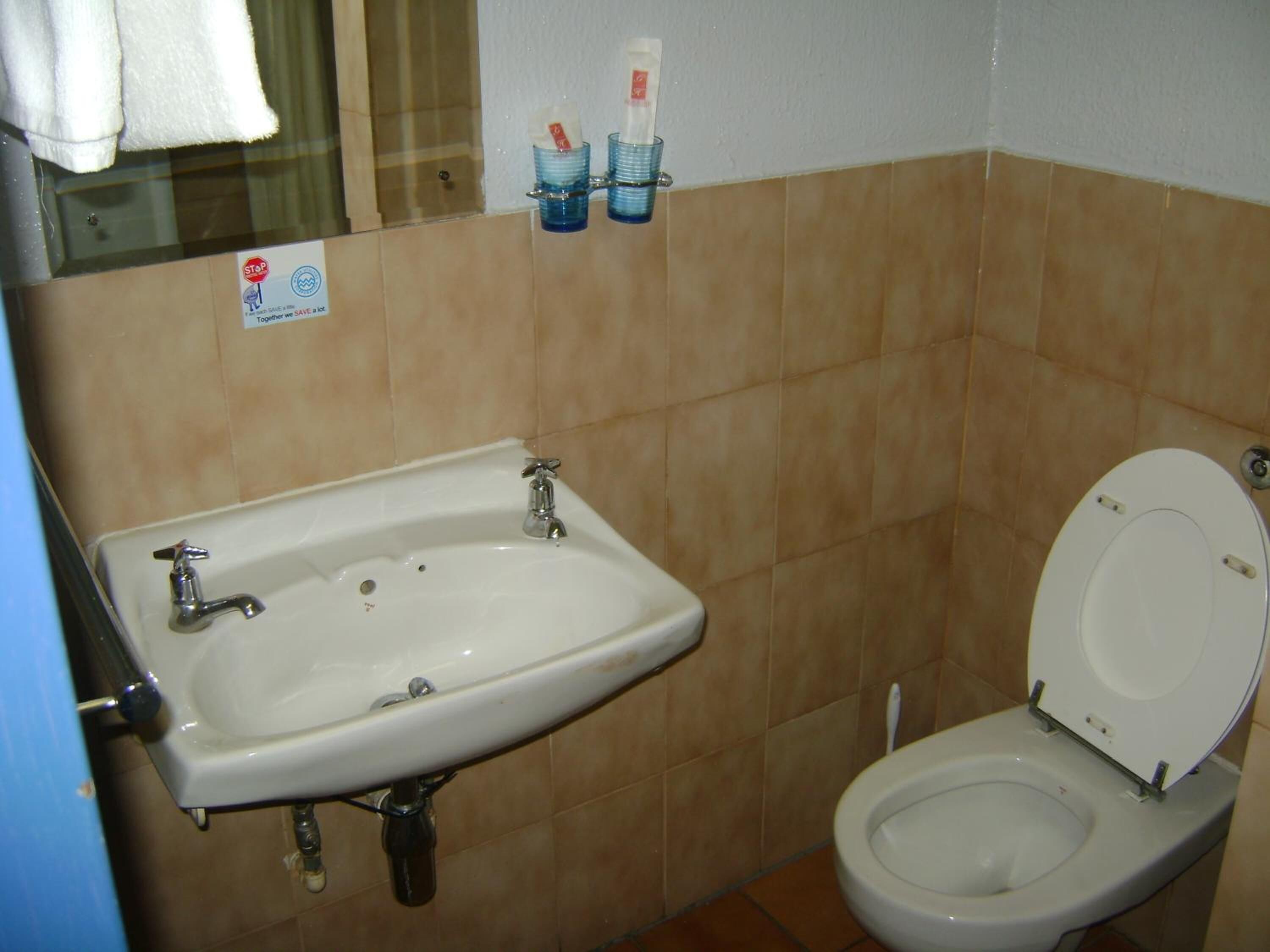 Un baño con lavamanos, inodoro, paredes con azulejos y una toalla colgada en una puerta.