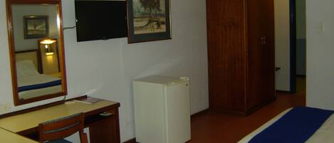 Habitación de hotel con cama, escritorio, silla, armario, espejo y televisor.