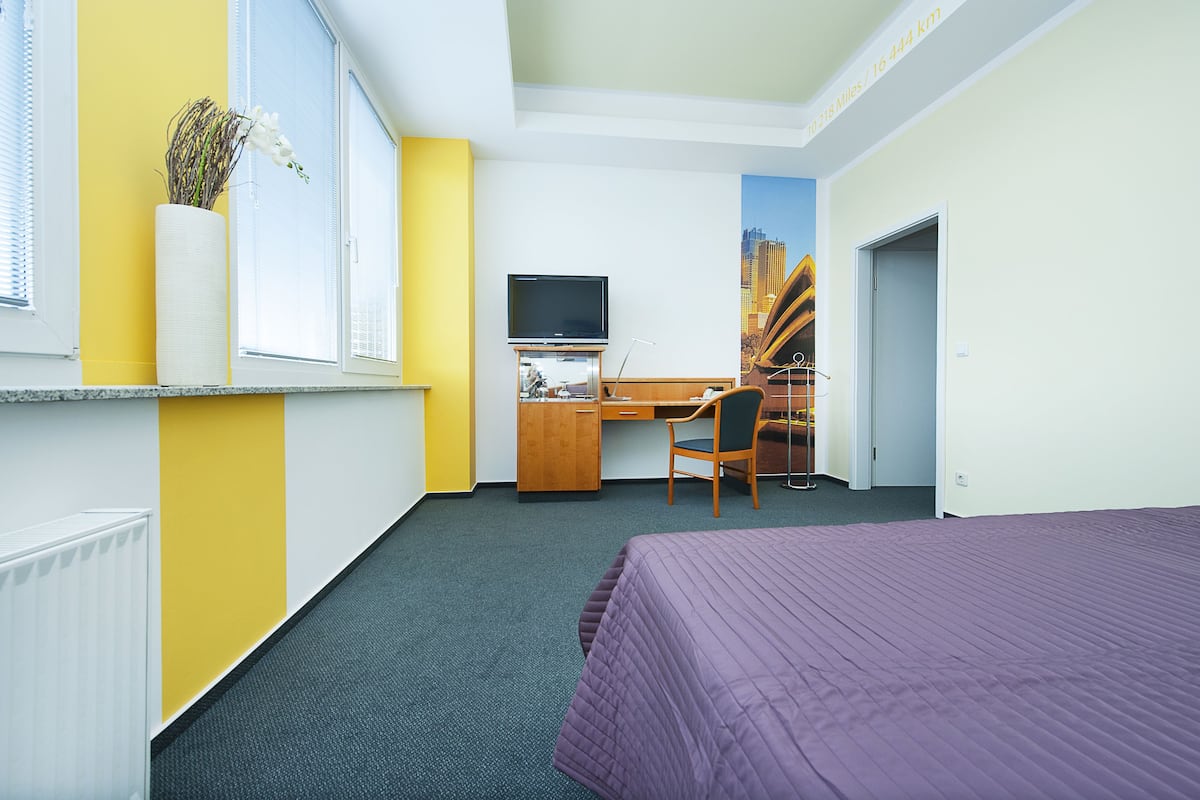 Habitación de hotel con cama, escritorio, silla, televisor y ventana con planta.