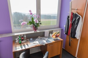 A desk with a vase of pink orchids, a bowl of fruit, and a newspaper. - Hotel Weitblick (Bielefeld)