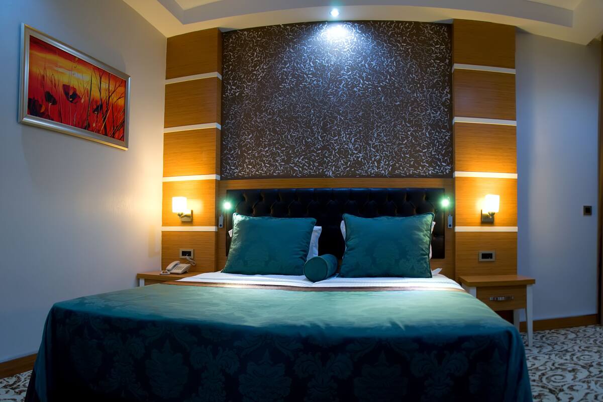 A hotel room with a large bed, two bedside lamps, a telephone, and a decorative wall panel.