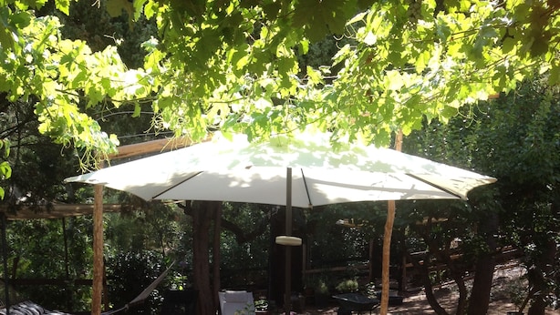 An outdoor patio with a table set for dining, surrounded by chairs, under a large umbrella. - La Casa delle Fate (Loiri Porto San Paolo)