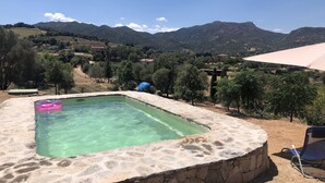 A stone pool with clear water, surrounded by a stone wall, and overlooking a mountainous landscape with trees and houses. - La Casa delle Fate (Loiri Porto San Paolo)
