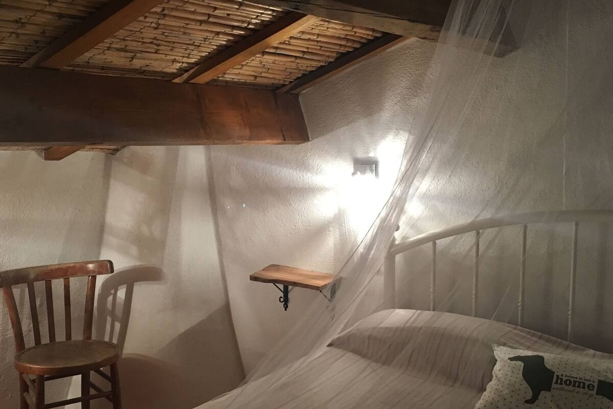 A bedroom with a bed, a chair, a shelf, and a mosquito net.
