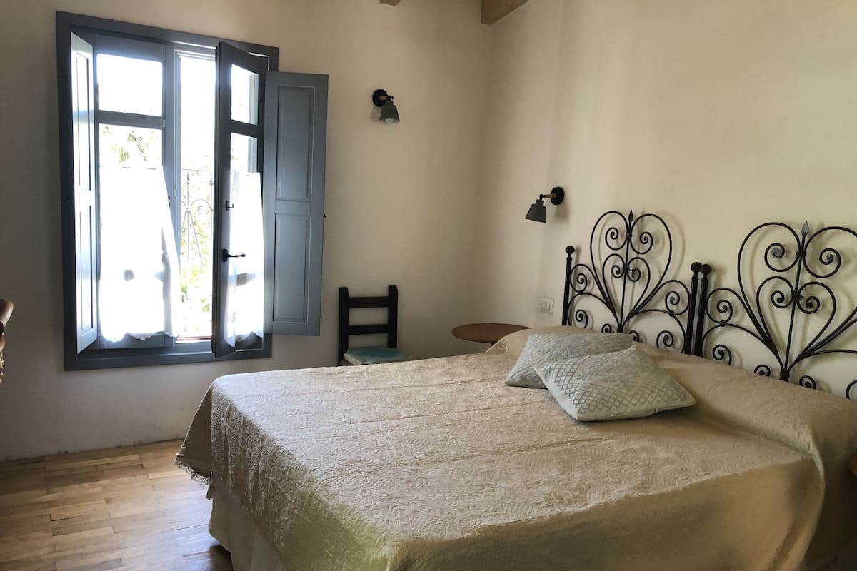 A bedroom with a bed, a chair, a small table, and a window with curtains.