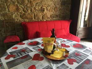A table with a red heart-patterned tablecloth, a bottle of wine, a bag of chocolate, and a tray with a knife and a heart-shaped item.
