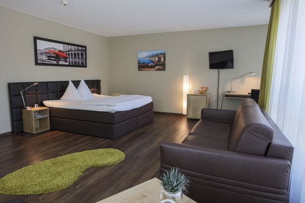 A modern hotel room with a large bed, a sofa, a desk with a TV, and artwork on the walls. - Herisau Swiss Quality Hotel (Herisau)