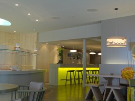 Zona de bar moderna con mostrador iluminado en verde, taburetes y una lámpara colgante.