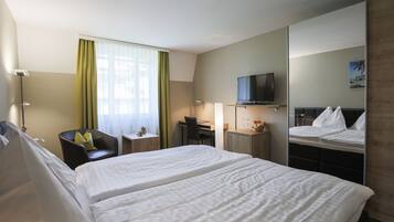 Habitación de hotel con dos camas, un escritorio, una silla, un televisor y un espejo.
