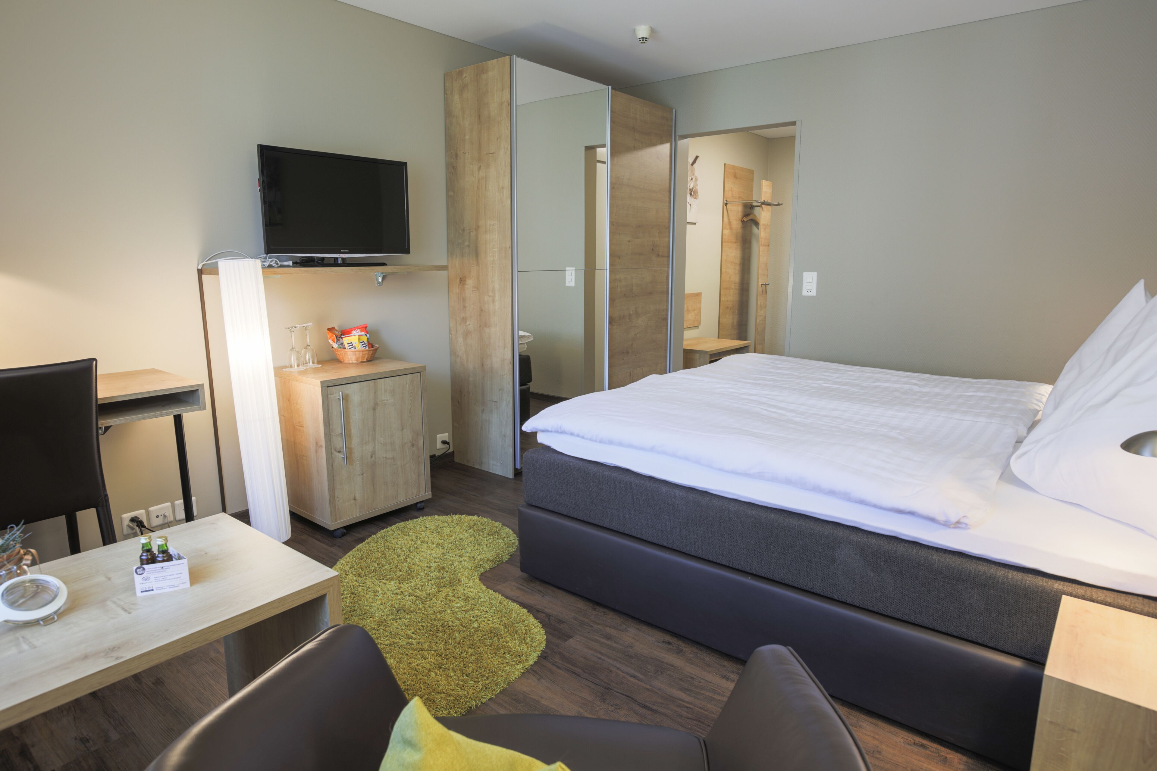 A modern hotel room with a bed, a desk, a television, and a mirror.
