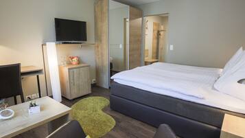 A modern hotel room with a bed, a desk, a television, and a mirror.