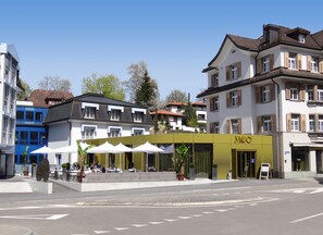 A street view with a cafe named "MOO" featuring outdoor seating and a yellow awning. - Herisau Swiss Quality Hotel (Herisau)