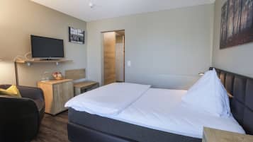 Een moderne hotelkamer met een groot bed, een flatscreen-tv bevestigd aan een houten plank, een klein bureau met een lamp en een schilderij aan de muur.
