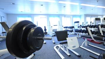 Un gimnasio con equipo de levantamiento de pesas, bancos y mancuernas.
