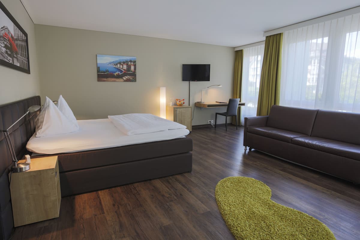 Una habitación de hotel con una cama, un escritorio con computadora, un sofá y un televisor en la pared.