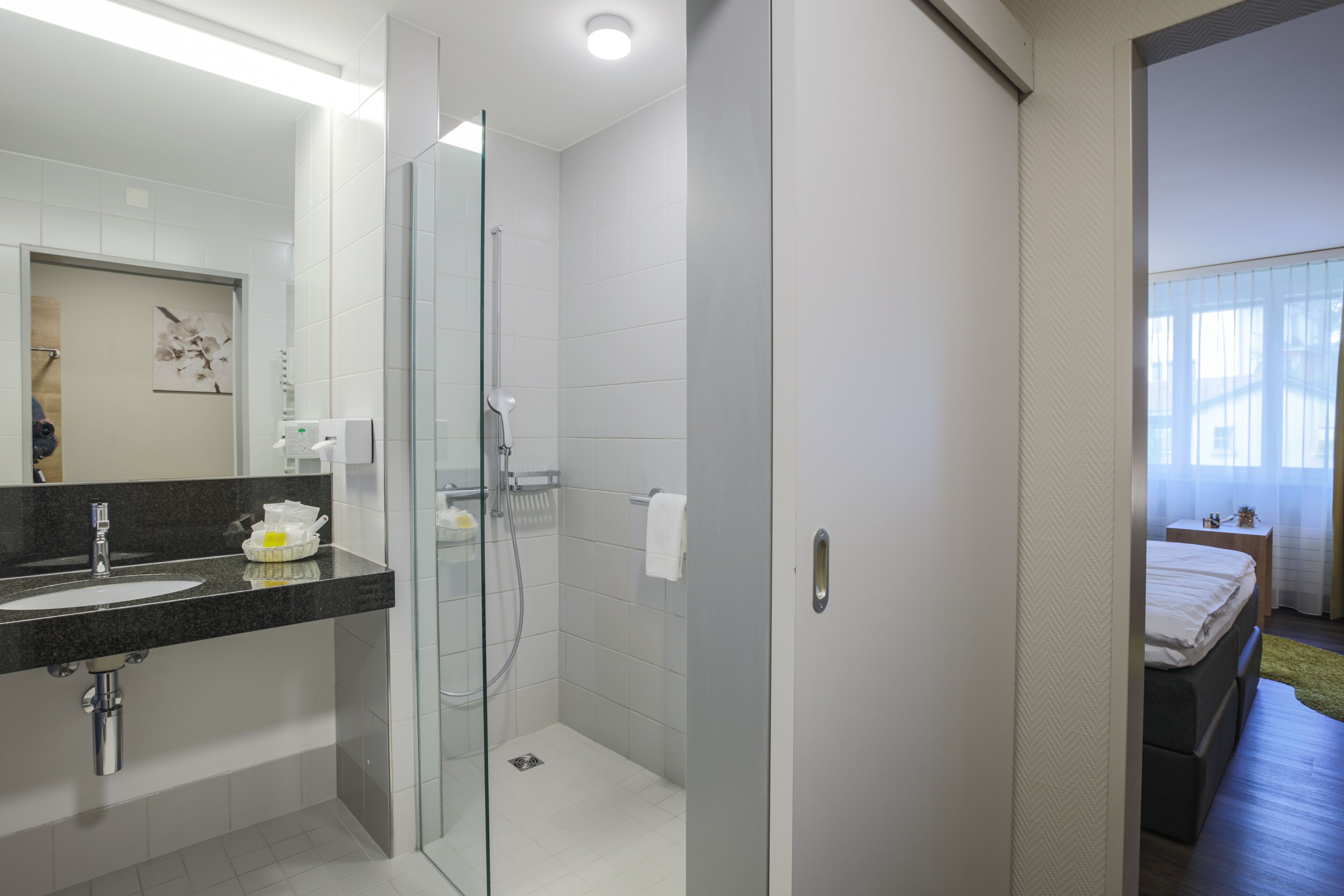 Une salle de bain moderne avec une douche à l’italienne en verre, un lavabo doté d’un plan de toilette noir et un porte-serviettes apparent.