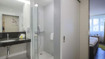 Une salle de bain moderne avec une douche à l’italienne en verre, un lavabo doté d’un plan de toilette noir et un porte-serviettes apparent.