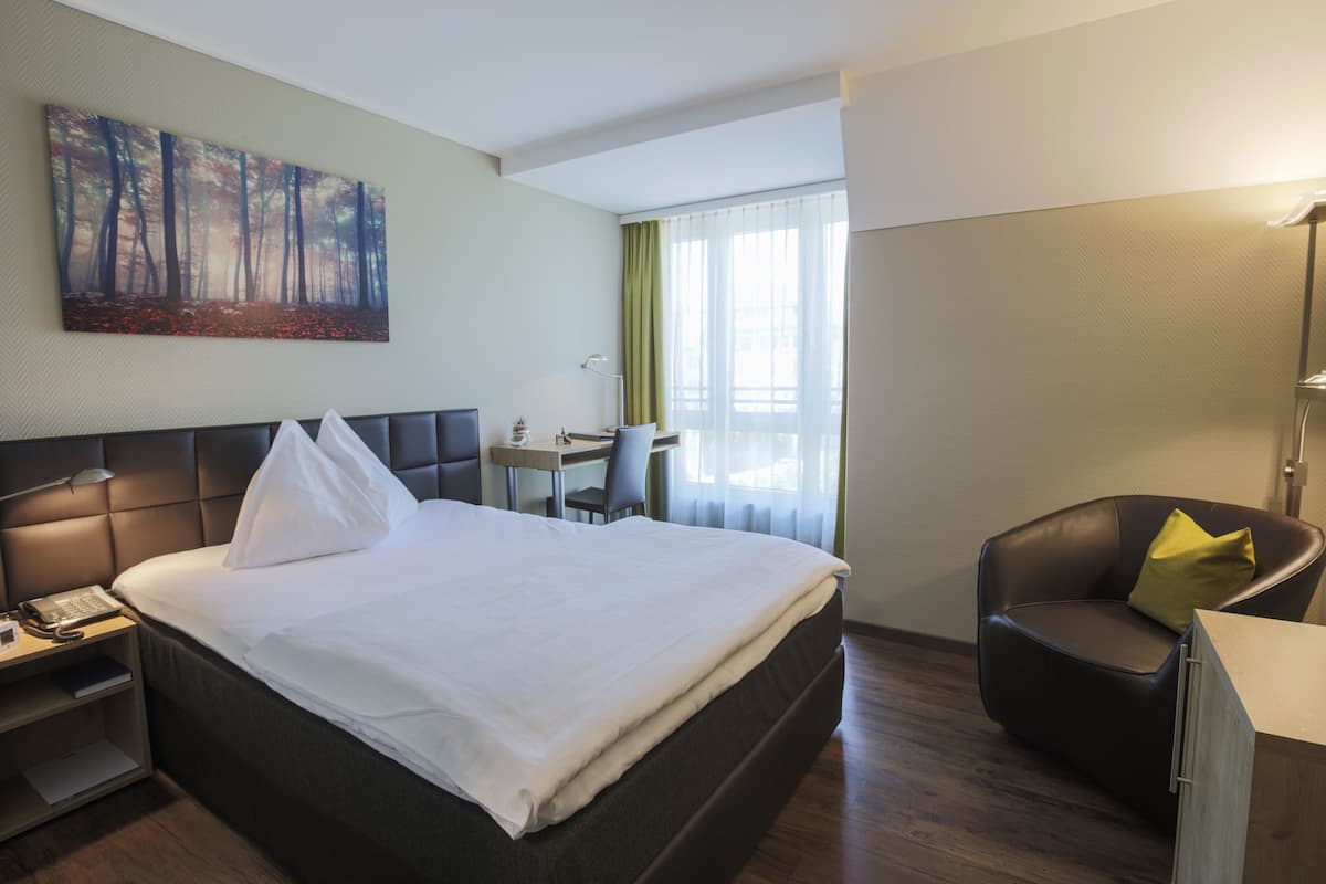 Una habitación de hotel con una cama grande, un escritorio, una silla y un cuadro en la pared.
