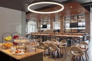 Uma área de jantar moderna com parede de tijolos, teto de madeira e diversos itens de café da manhã à mostra.