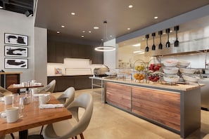 A modern kitchen with a central island, overhead lighting, and a dining area with chairs and a table.